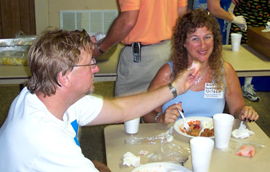 Nancy sits down to eat after taking pictures, and hubby Darrell tempts her with cake